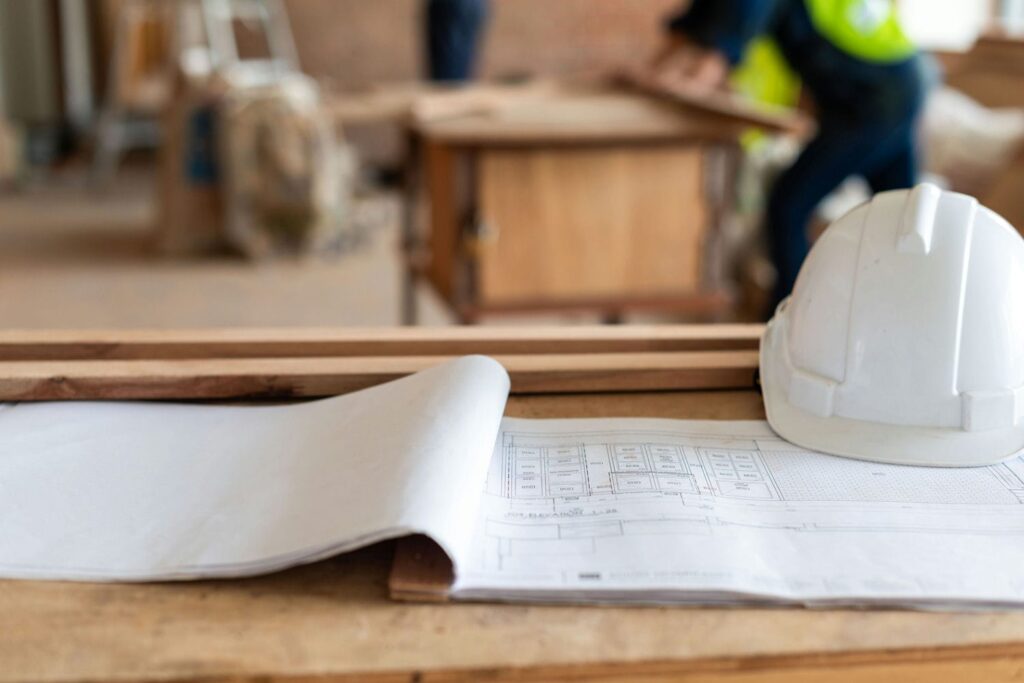 Architectural drawings and hard hat on a job site representing the pricing and scope questions builders should ask before starting a custom home