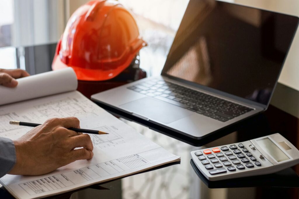 Contractor reviewing blueprints with a calculator and laptop while estimating exterior finishing labour costs.