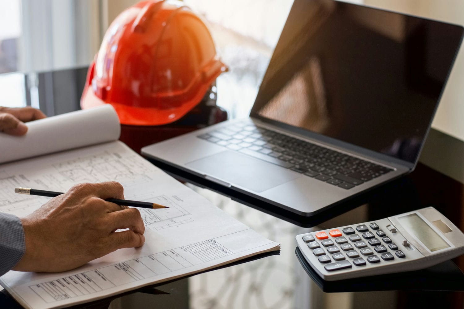 Contractor reviewing blueprints with a calculator and laptop while estimating exterior finishing labour costs.