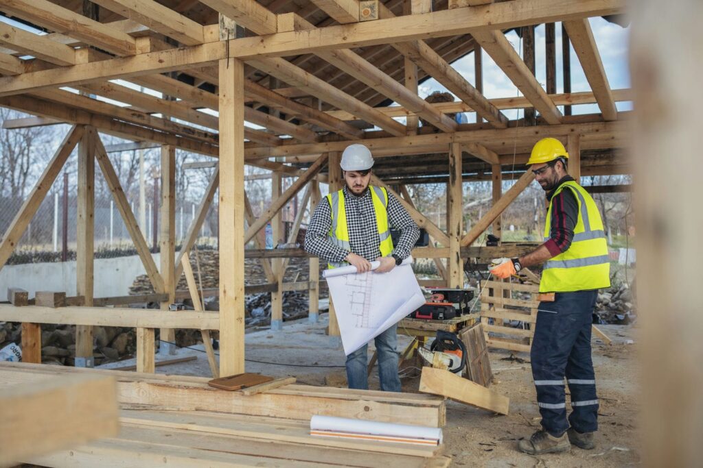 Framing contractor and crew member reviewing structural drawings on a wood-framed custom home construction site