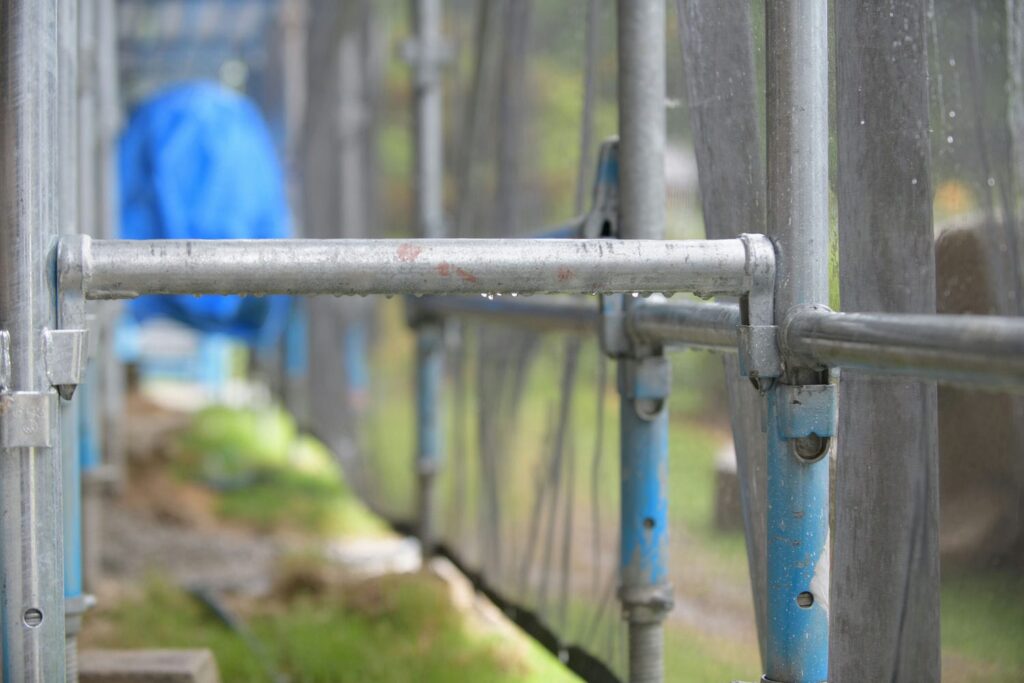 Wet scaffolding with rain droplets and protective mesh sheeting on an exterior finishing job site during rainy weather.