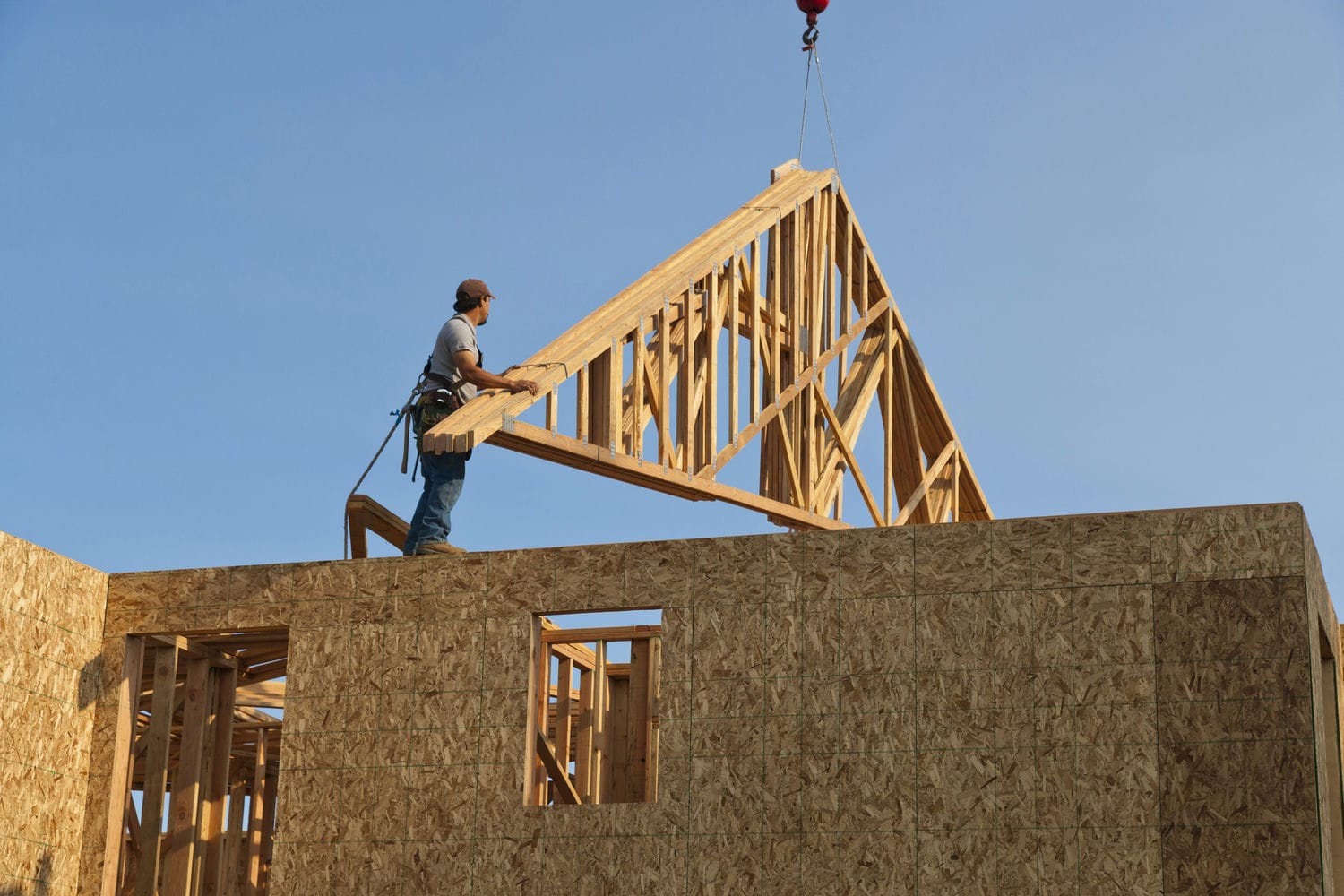 Stick-framed custom home with roof trusses being installed representing traditional site-built framing methodology