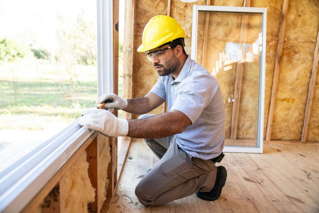 Window installer measuring an opening on a custom home representing finish trades most affected by out-of-square framing