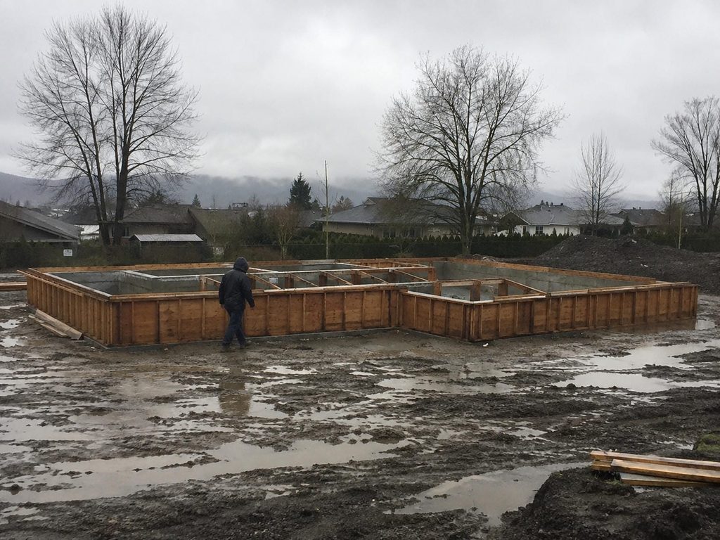 Residential foundation still in its forms during winter rain on a Metro Vancouver building site