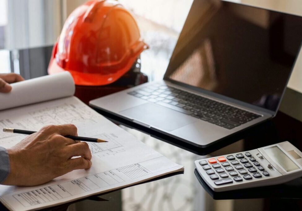 Contractor reviewing blueprints with a calculator and laptop while estimating exterior finishing labour costs.