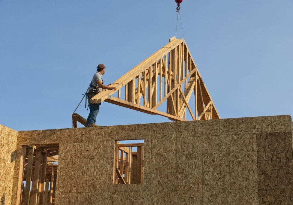 Stick-framed custom home with roof trusses being installed representing traditional site-built framing methodology