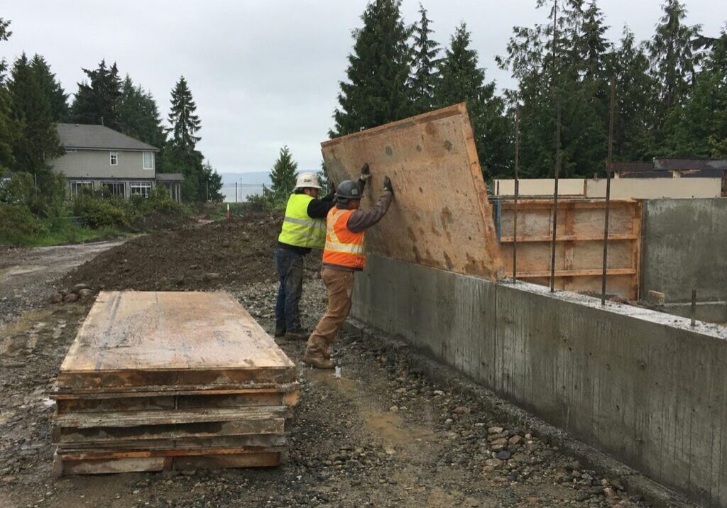Carpentry crew removing concrete forms from a new residential foundation on a wet Metro Vancouver site